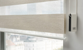 Modernes Twinrollo mit beige-weißen Streifen vor Stadtblick – lichtdurchlässiger Sicht- und Sonnenschutz für Fenster, Innenraumgestaltung mit Kettenzug